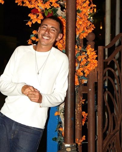 Robin Rainero, sourire, pull blanc, devant une vigne de fleurs orange à Nice
